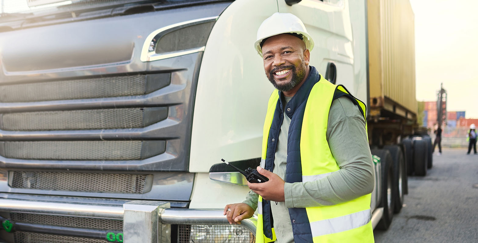 a smiling worker with safety work uniform standing in front of a truck